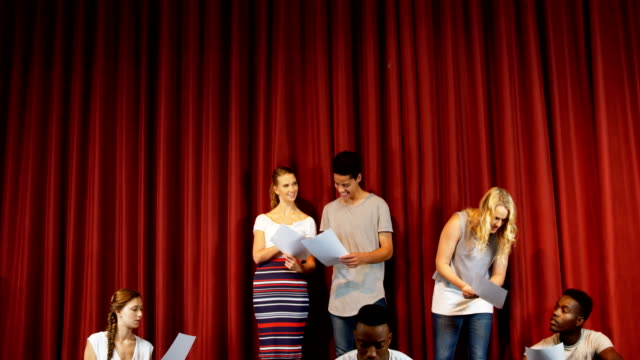Image of a group of teens reading scripts in front of a theater curtain.