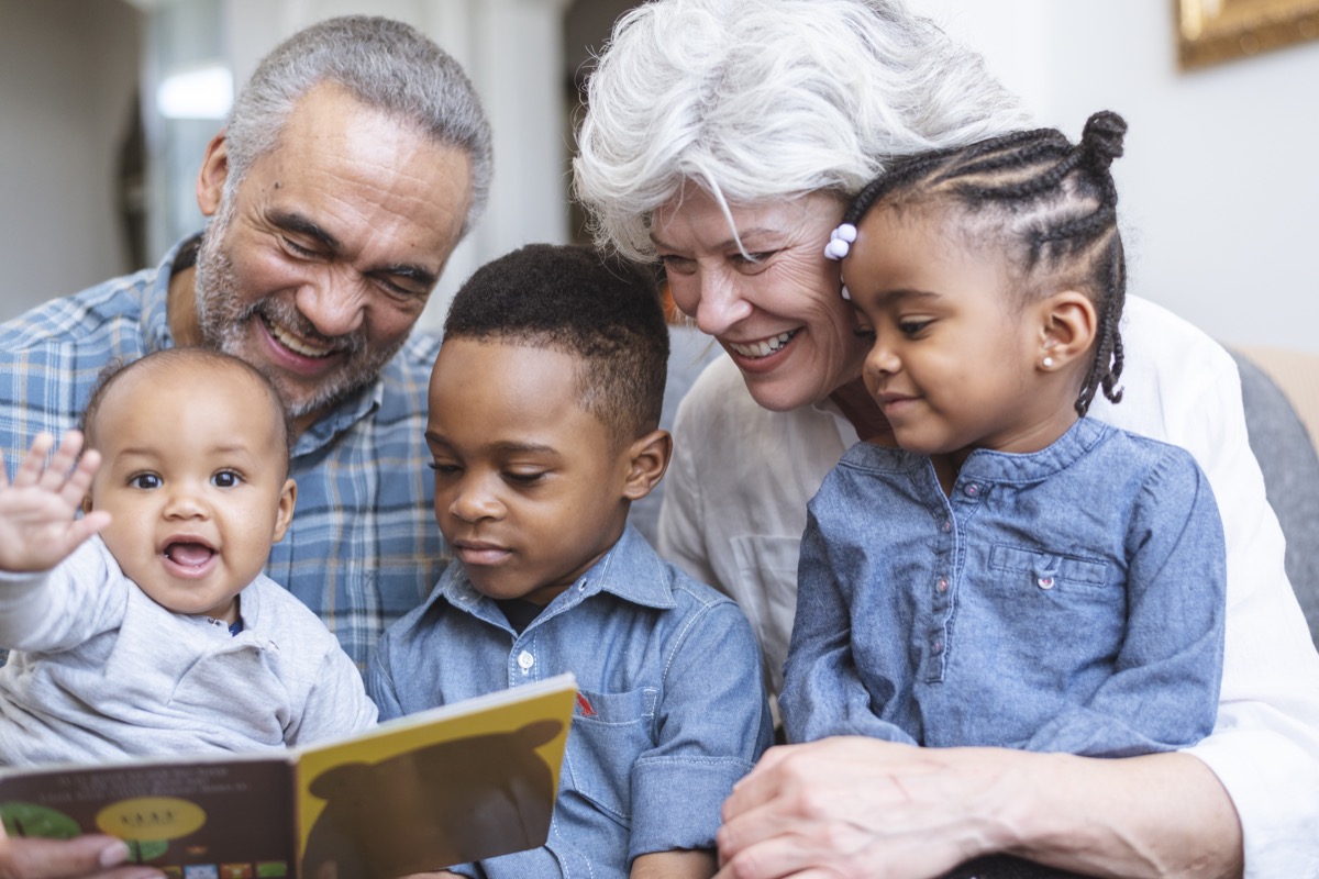 Photo of two grandparents reading a picture book with their young grandchildren.
