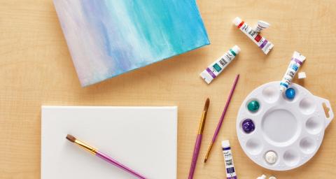 Image of a partially-painted canvas, a blank canvas, and surrounding art supplies.