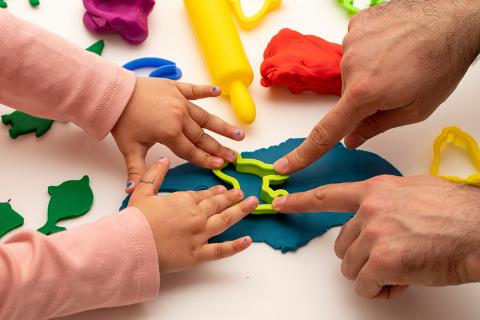 Child's hands and adult hands playing with colorful clay.