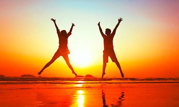 Image of two people jumping silhouetted by a sunset on the beach.